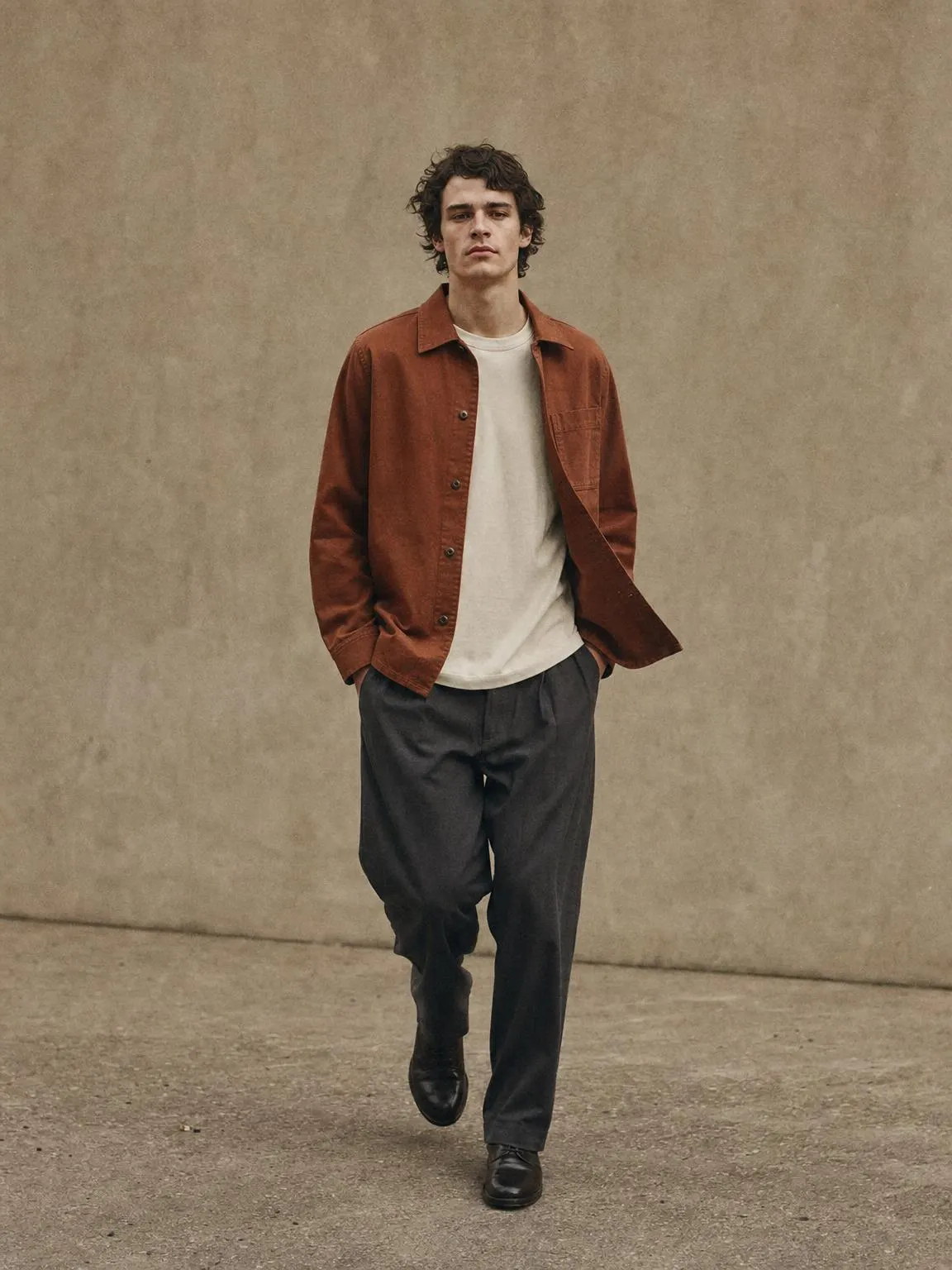 A boxy cotton-twill overshirt in muted terracotta worn open.
