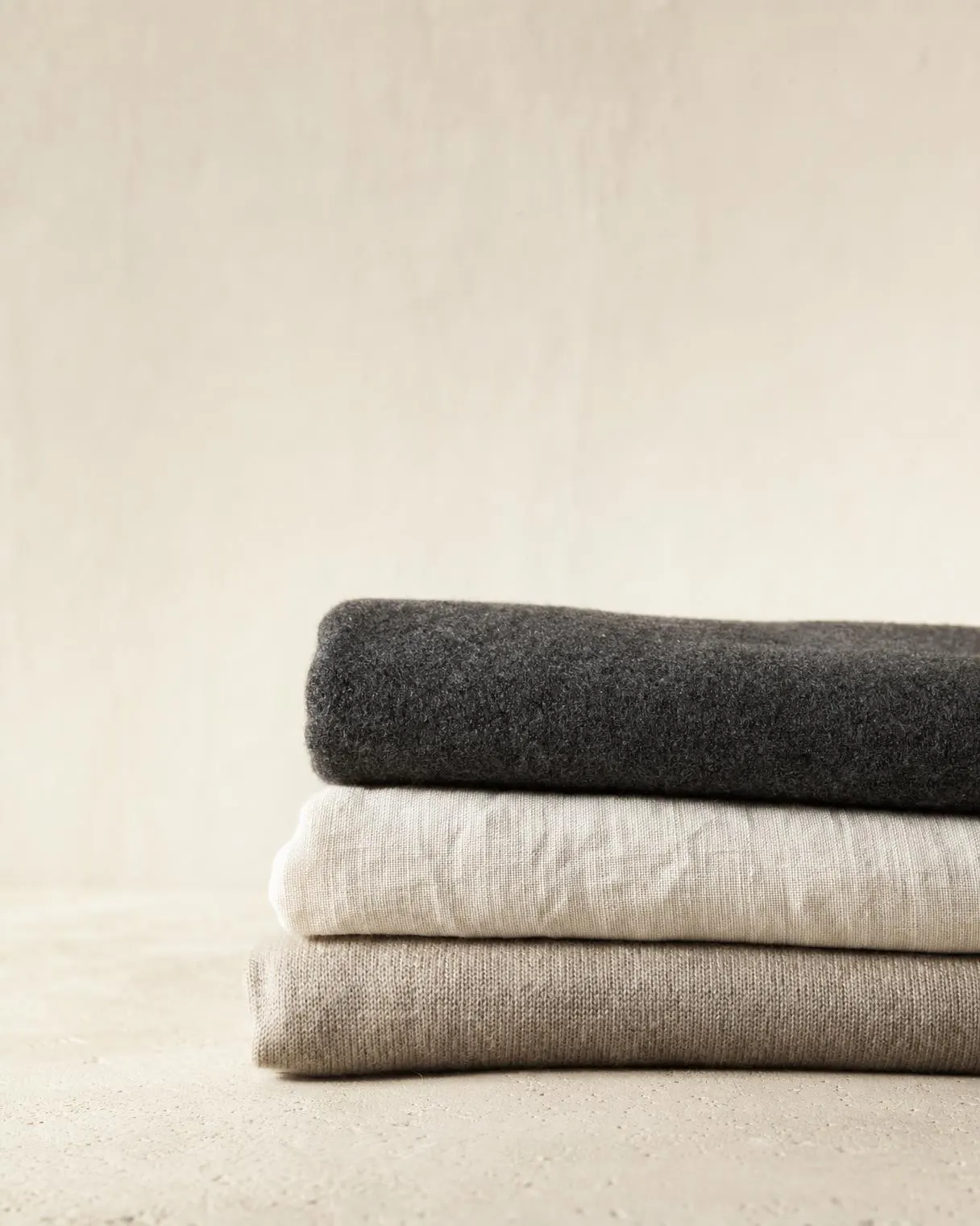 Three folded lengths of cloth: charcoal wool, washed linen and undyed merino.