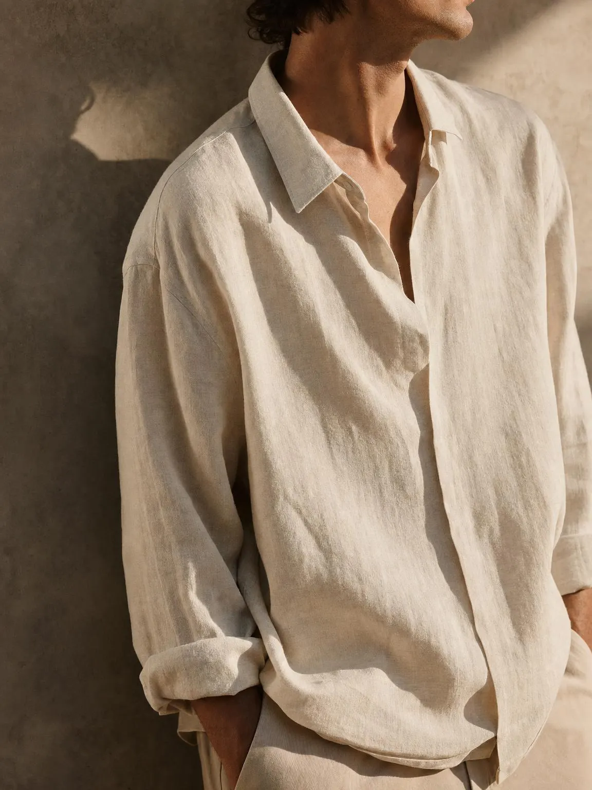 An oversized washed linen shirt in warm off-white, sleeves rolled once.